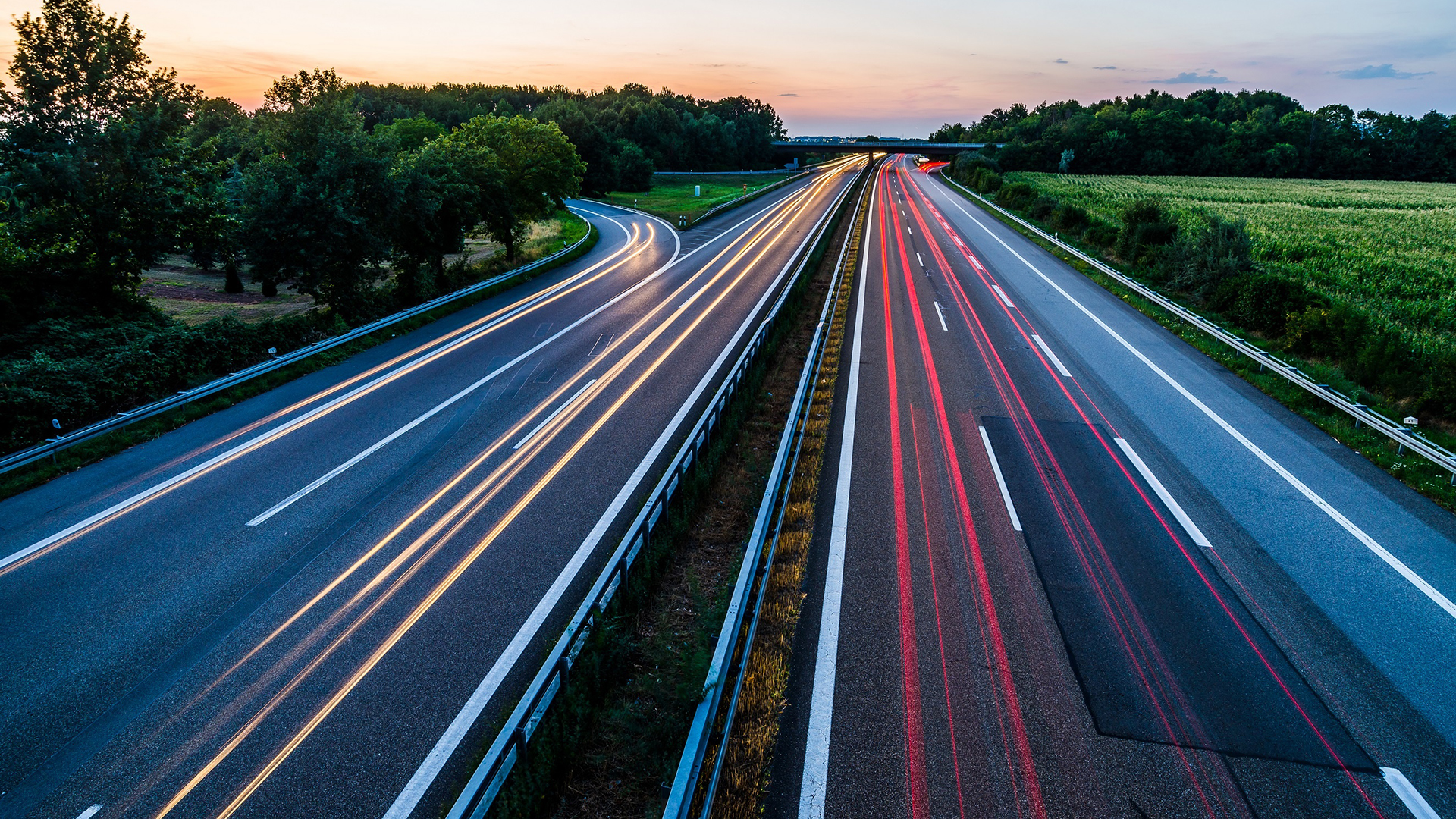 Two-lane highway with greenery and car lights at dusk