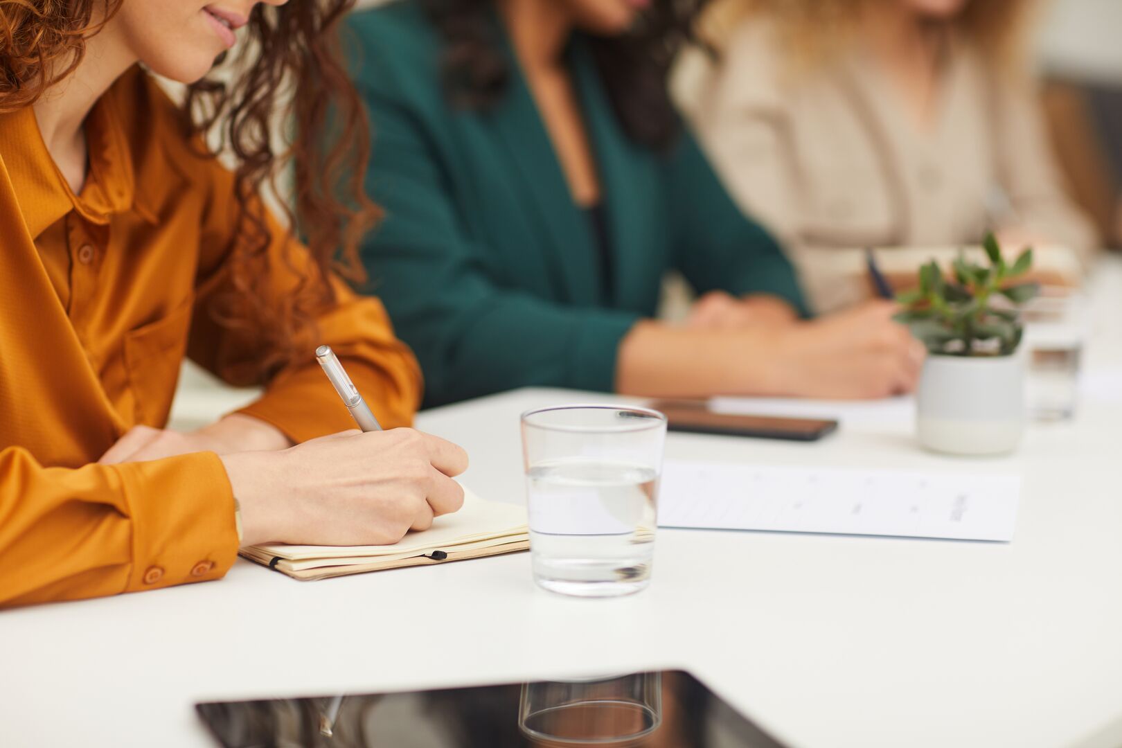 Horizontal shot of three unrecognizable young women sitting together at office table making notes