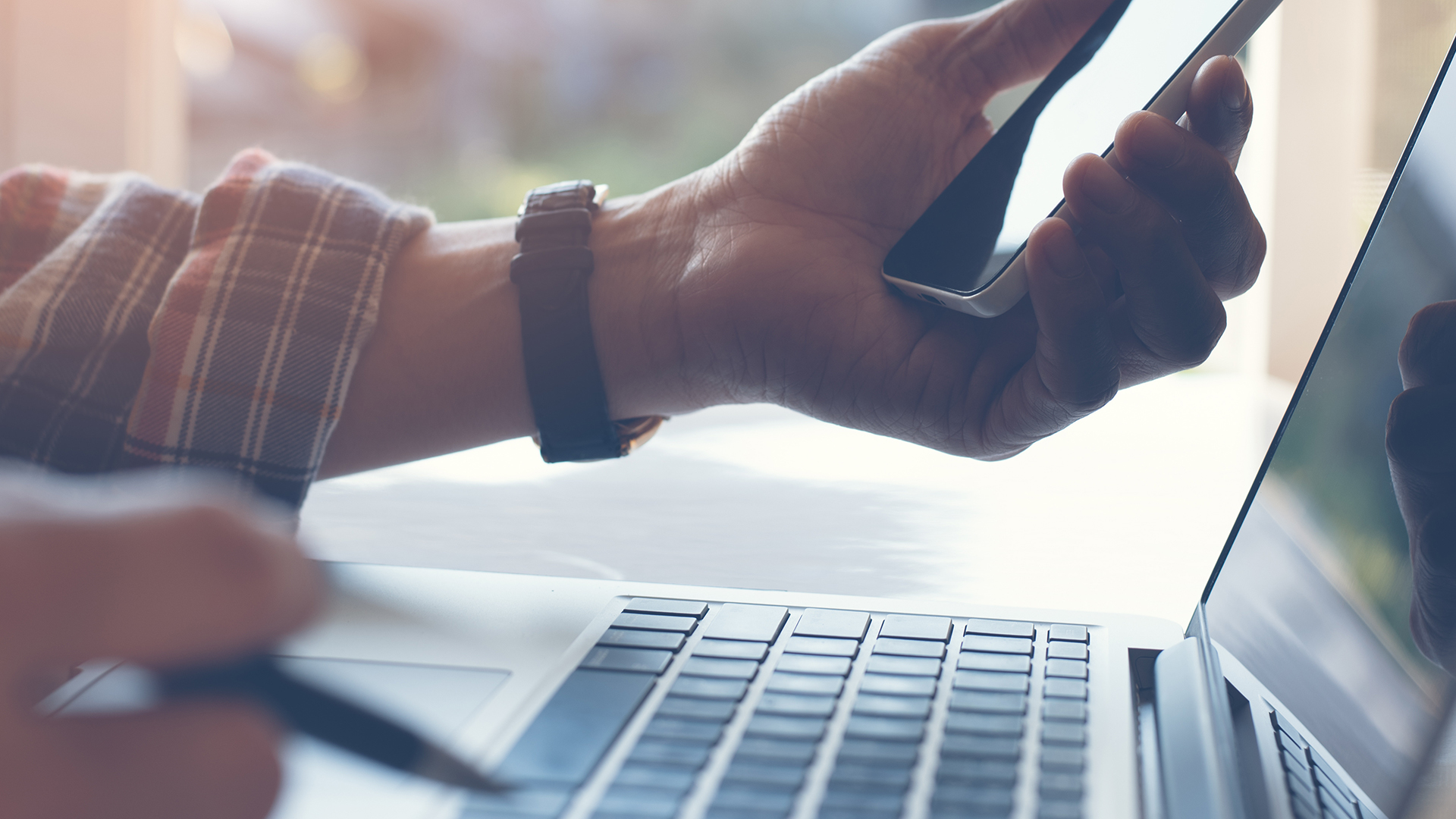 hand holding a phone and pen with laptop