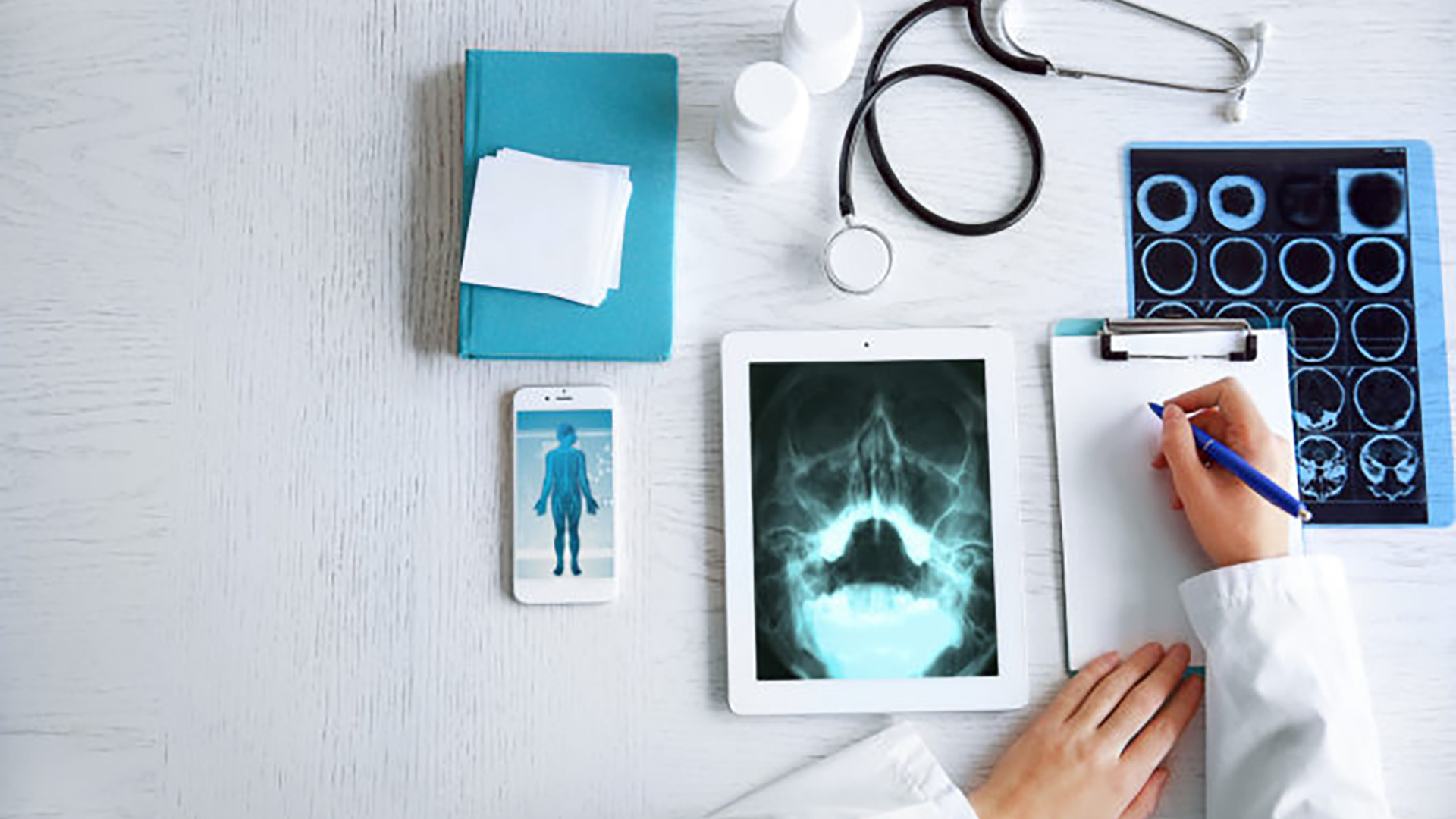 Doctor in white coat writing on legal pad with medical devices and notes on table