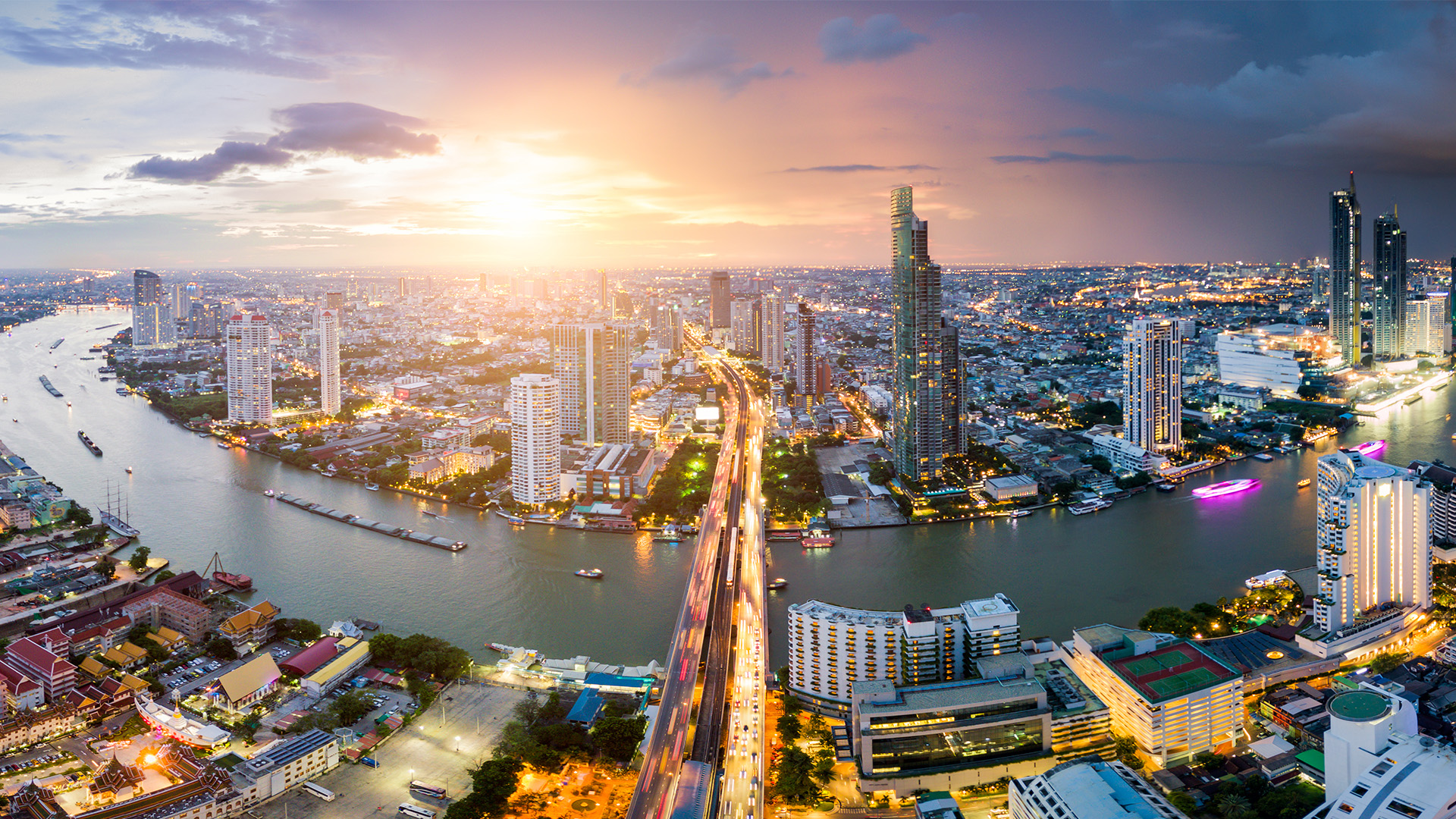 Aerial view of Bangkok skyline and skyscraper with light trails on Sathorn Road center of business in Bangkok downtown. Panorama of Taksin Bridge over Chao Phraya River Bangkok Thailand at sunset