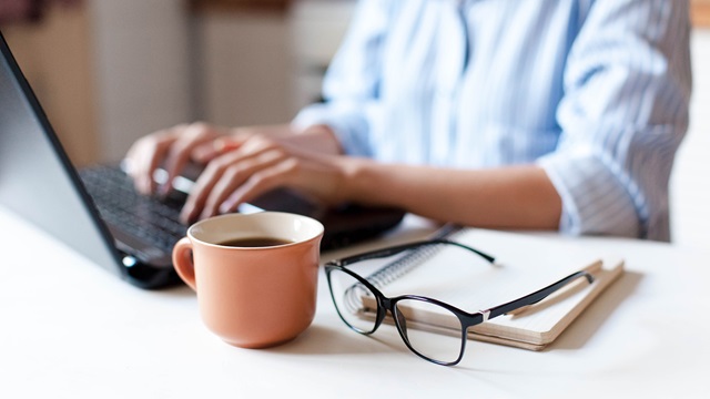 Typing on laptop with glasses nearby