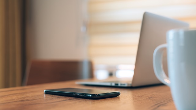 Employee workstation with a phone, laptop and coffee mug on the desk