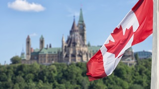 Canadian flag waving with Parliament Buildings hill and Library