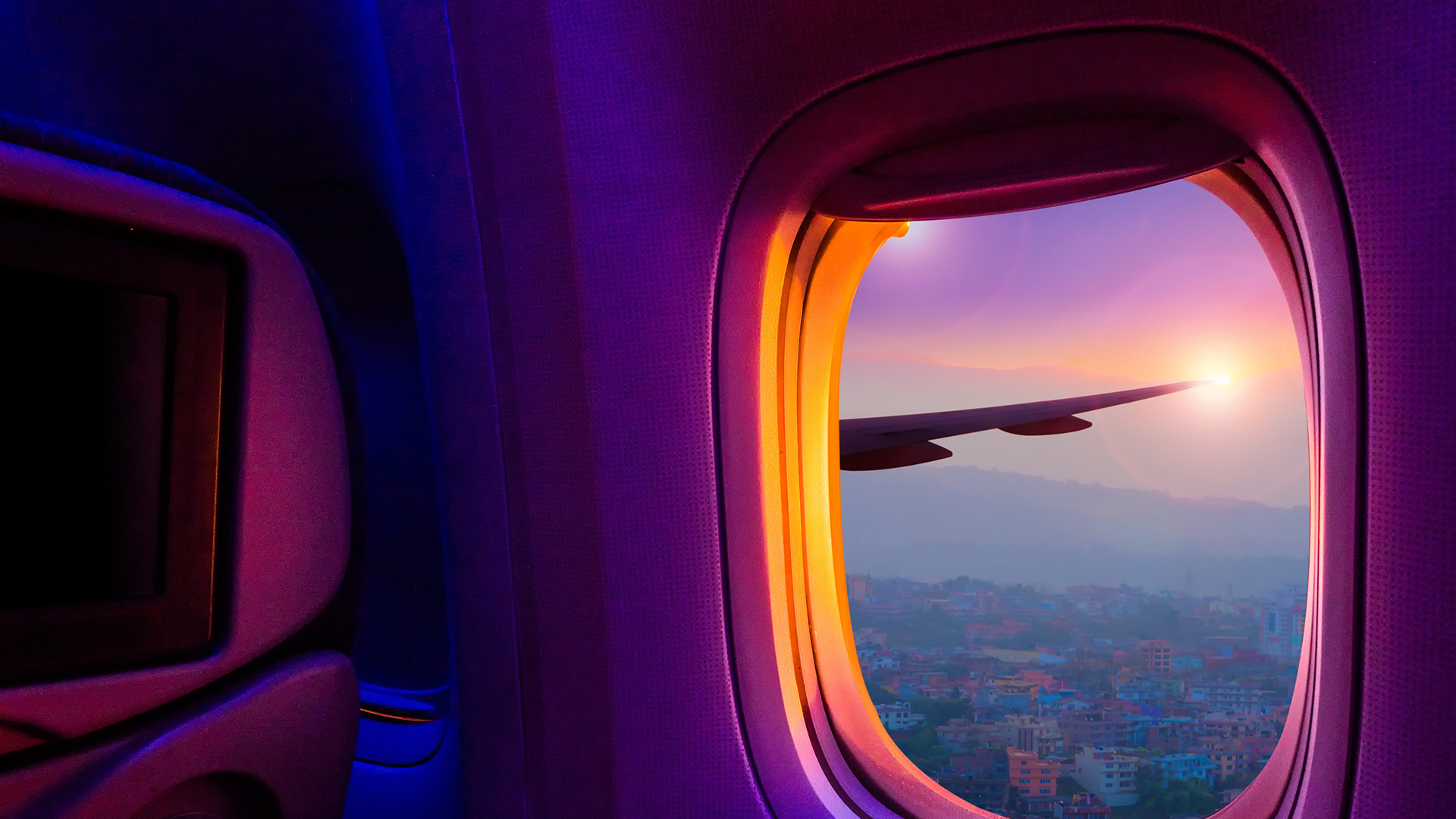 Airplane seat and open window looking out onto the wing and sunset