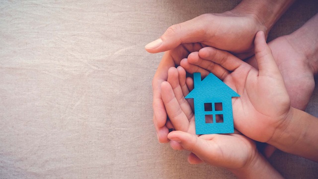 Two sets of hands holding a blue cutout of a home