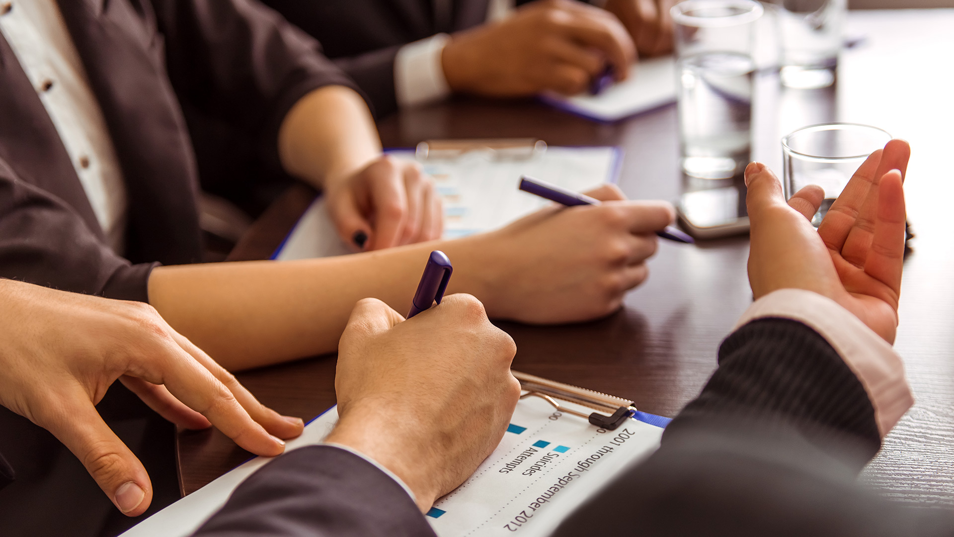 Close-up of people's hands holding pens on meeting table