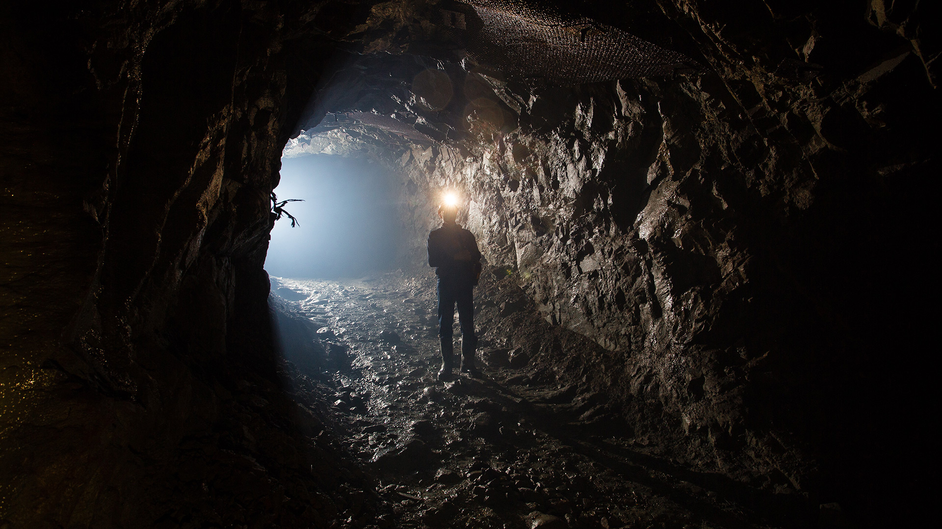 Un mineur dans un tunnel de mine avec sa lampe frontale allumée