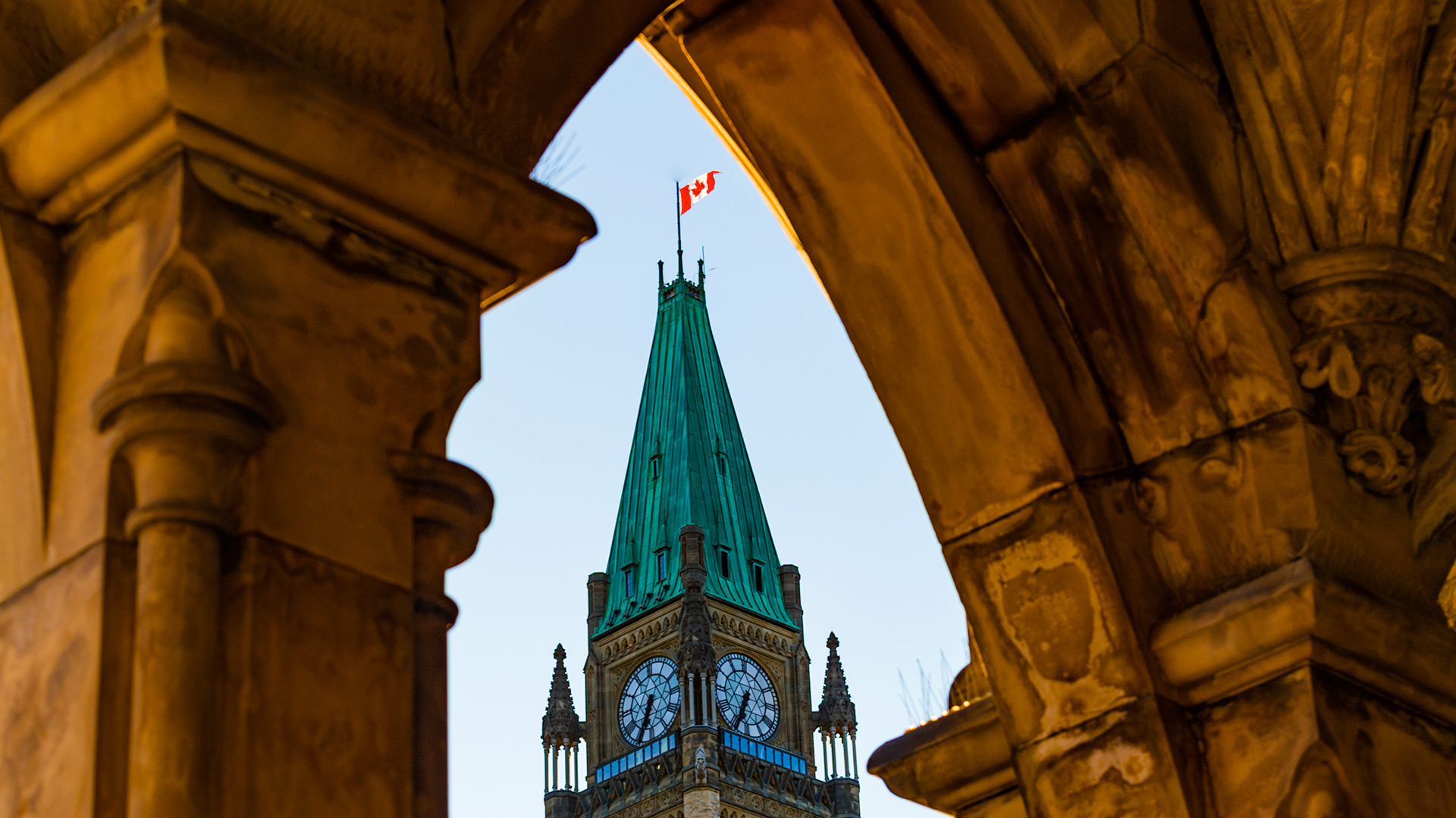 Canadian flag on top of Parliament building peeking through arch of other building