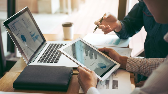 Two employees reviewing financial charts on a tablet and laptop