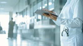 A doctor in a whitecoat holding a tablet in a hospital hallway