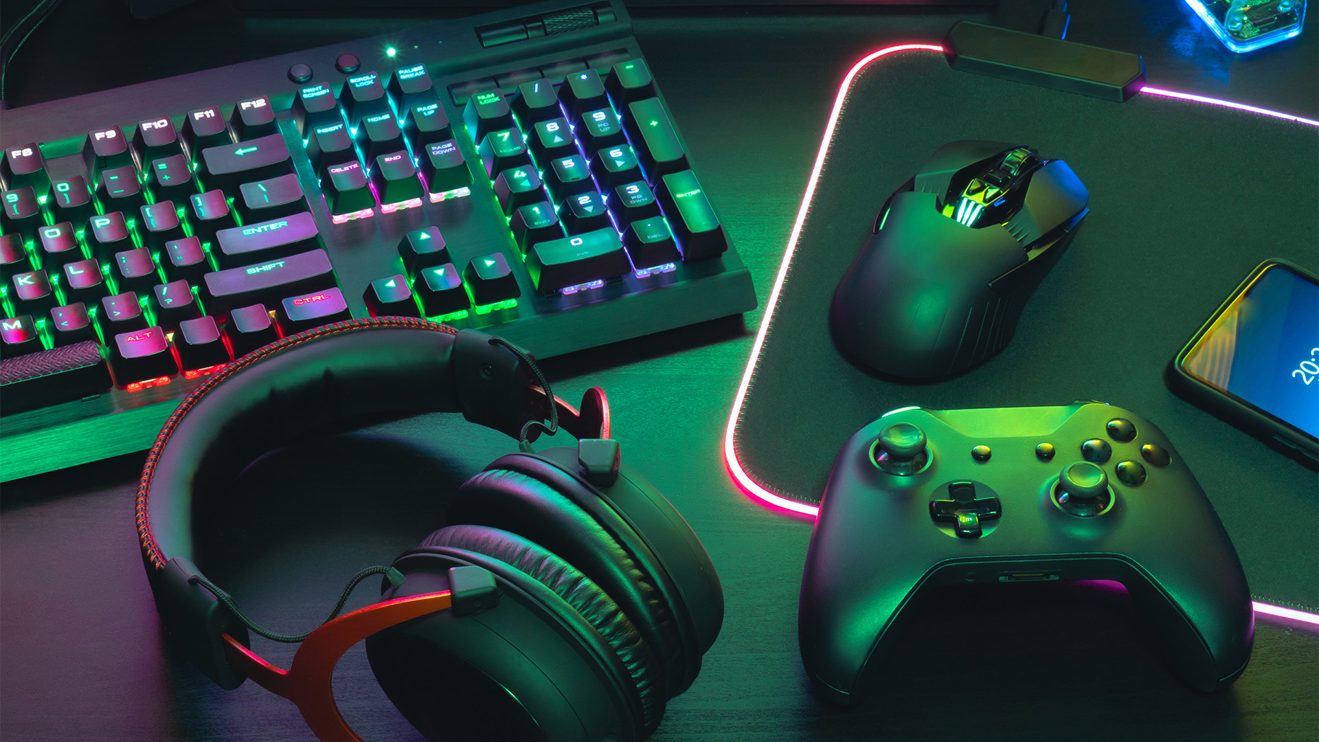 Online gaming desk setup with mouse, controller, headphones and keyboard with neon lighting