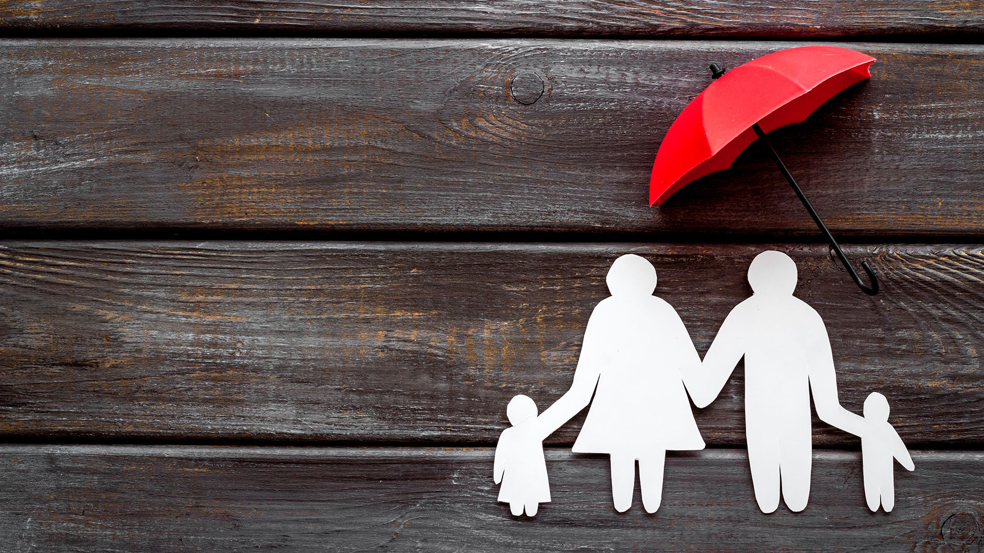 An white outlined silhouette of a family on a wood backdrop holding a red umbrella