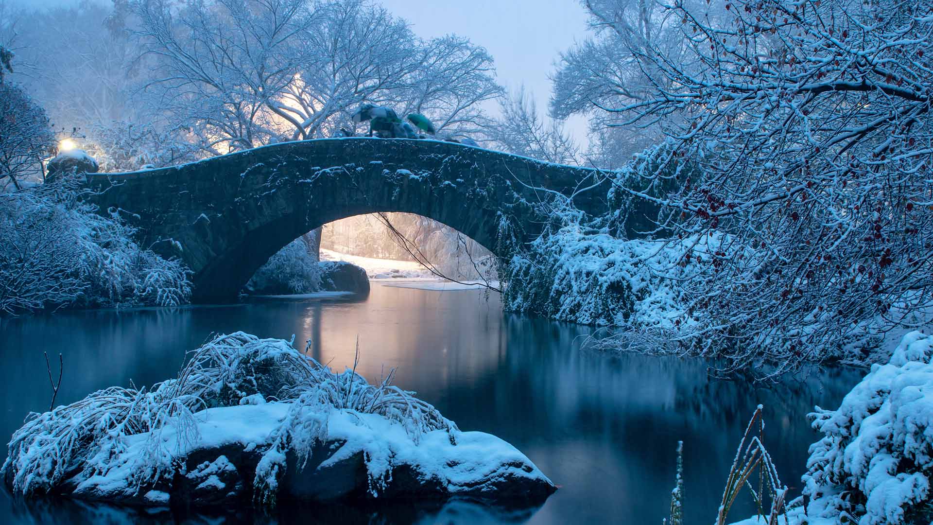 A snow-covered landscape with water running under a bridge in the United States